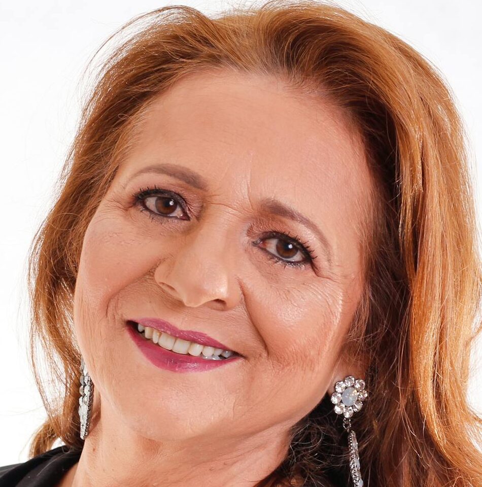 Portrait of a smiling senior woman with long hair and earrings in a black outfit.